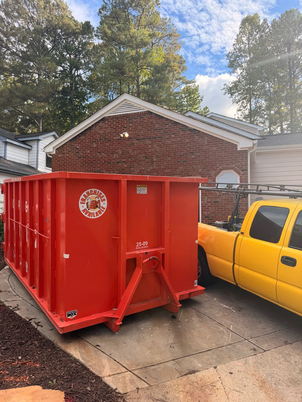 Red roll-off dumpster in the driveway during tear-out, next to a yellow work truck