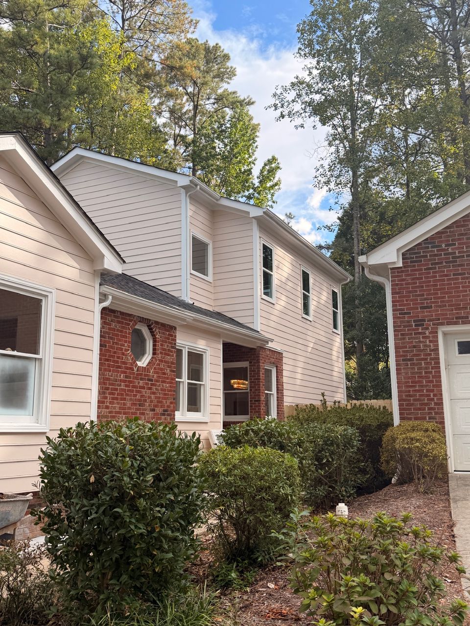 Two-story house with tan siding and brick, finished, with trimmed shrubs in front